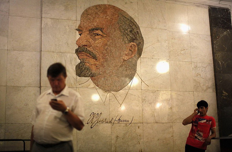 Men use their mobile phones as they stand in front of a mosaic depicting former Soviet leader Lenin at Biblioteka Imeni Lenina m